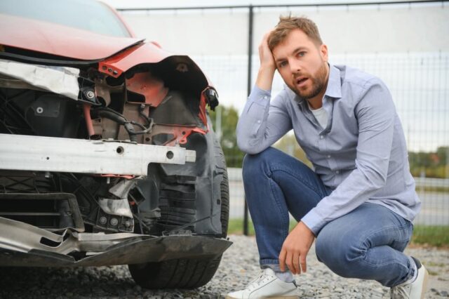 Man standing beside damaged car, reflecting on the aftermath of a car accident in Fayetteville.