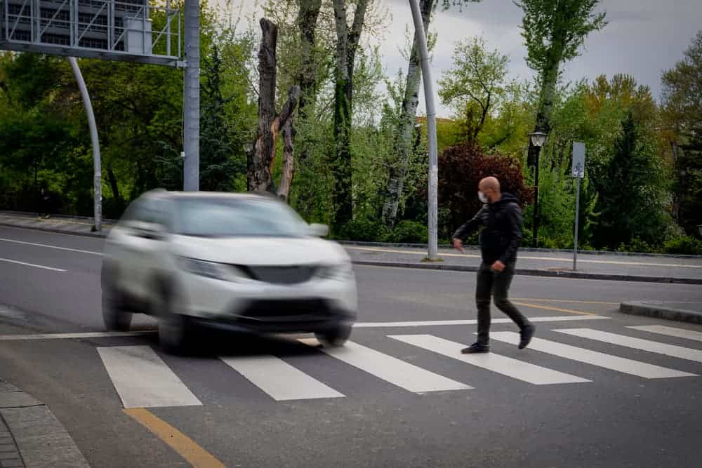Pedestrian walking on zebra crossing and a driving car failing to stop in blurred motion. Pedestrian reacts with hand to the driver.