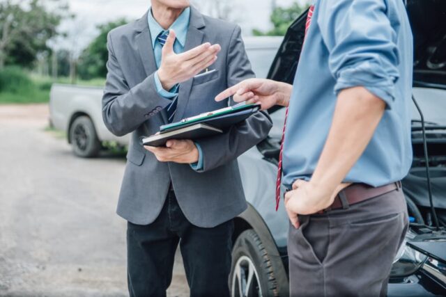 Insurance agent inspecting a damaged car and reviewing a claim form with a customer after an accident. The agent processes the claim and discusses payment details, illustrating the accident and insurance claim process.