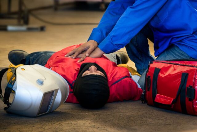 Worker receiving first aid after fainting in a factory. Safety gear used during industrial welding accident.