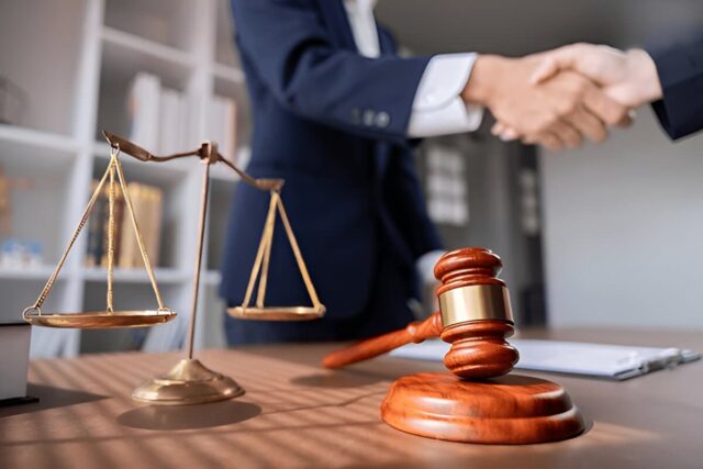 Lawyer handshake with justice scales and gavel, symbolizing legal agreement and partnership in a modern office setting.