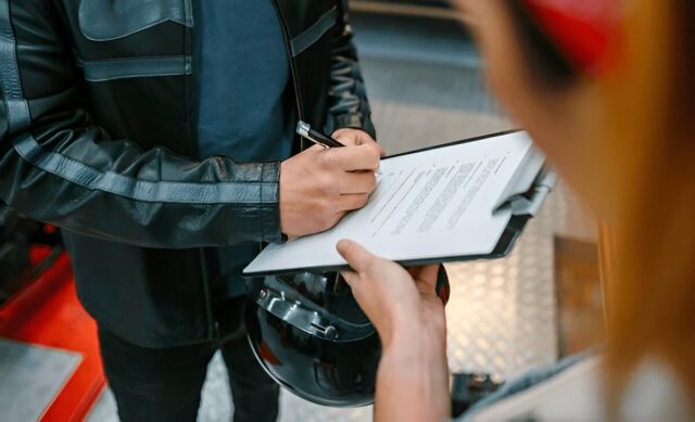 Biker signs insurance papers to collect repaired motorcycle at workshop.