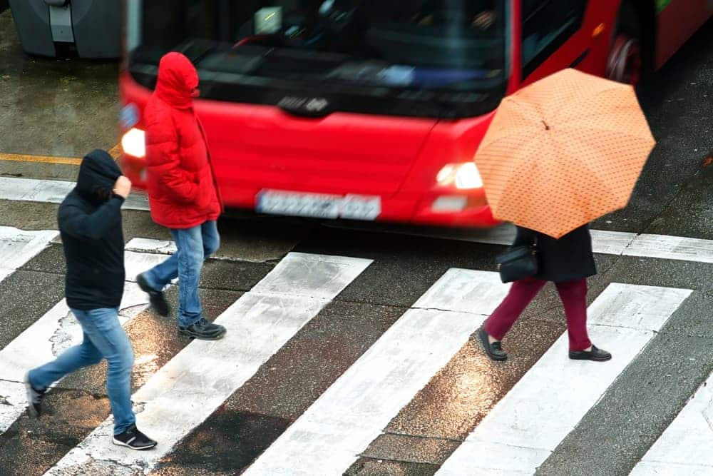 Pedestrians crossing wet crosswalk near a bus