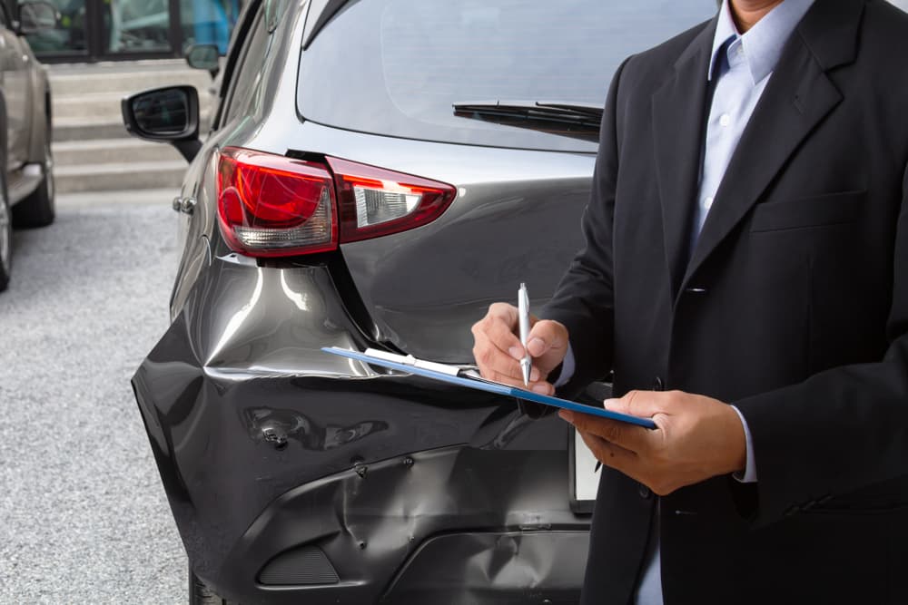 Un empleado de seguros toma nota de los detalles mientras un agente inspecciona un automóvil