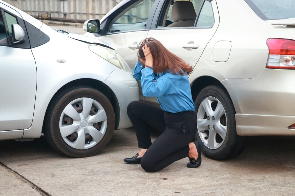 Distressed woman kneeling by two crashed cars