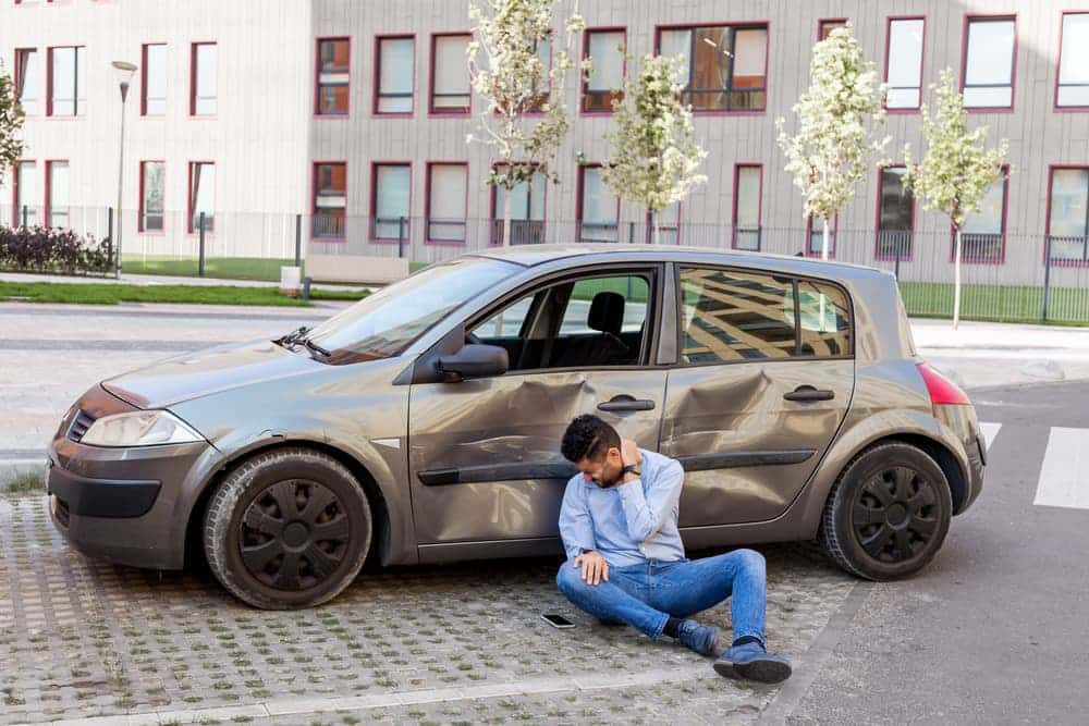 Injured man sits near wrecked car